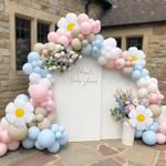 Arche de ballons pastel rose, bleu et beige avec grandes fleurs marguerites blanches pour décoration de baby shower ou anniversaire.
