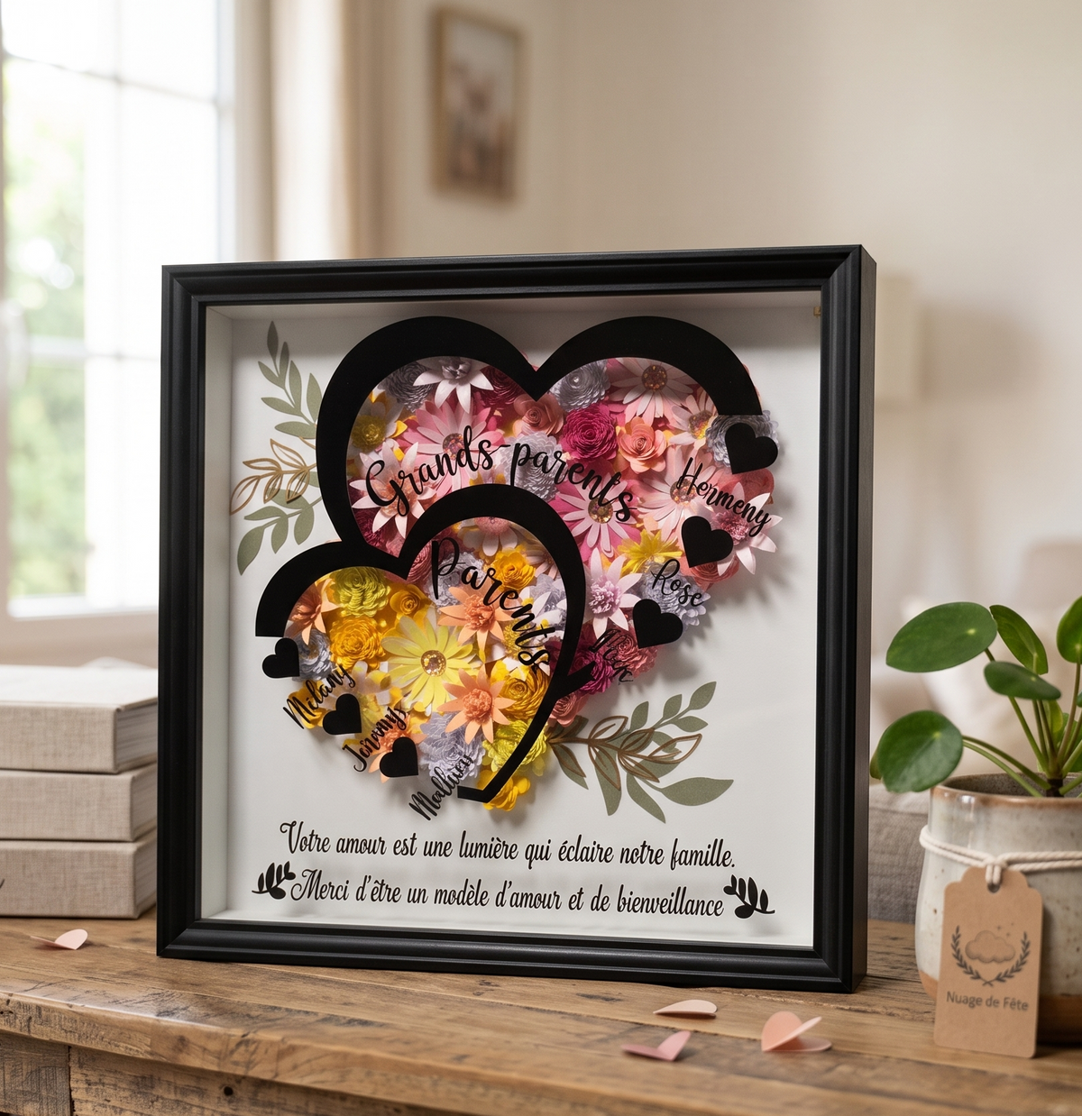 Vue de dessus de l'établi d'un artisan. Des mains masculines utilisent des pincettes pour assembler méticuleusement un cadre shadow box noir. Des bols de fleurs de papier colorées, des rouleaux de papier, de la colle, et des outils de précision sont éparpillés sur la table en bois. Un autre cadre terminé est visible en arrière-plan.