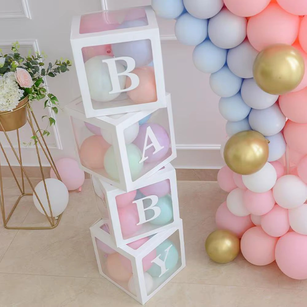 Pile verticale de boîtes de décoration 'BABY' transparentes et remplies de petits ballons multicolores pastel (rose, bleu, lavande, pêche). Les boîtes sont intégrées dans une arche de ballons pastel rose et bleu pour une fête Gender Reveal, avec des touches de doré.