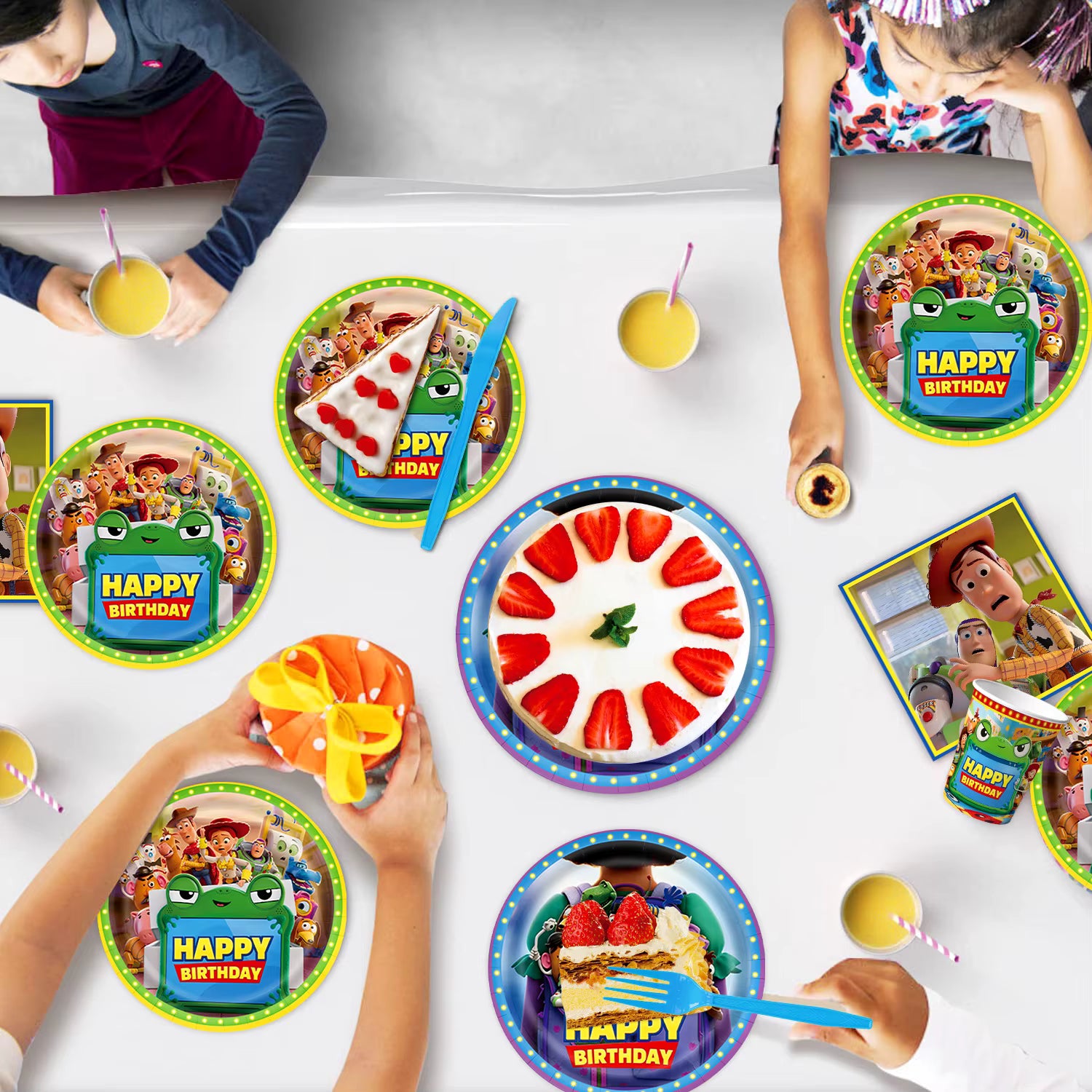 Enfants partageant un gâteau d'anniversaire sur une table décorée avec des assiettes et gobelets en carton sur le thème de l'univers des jouets.
