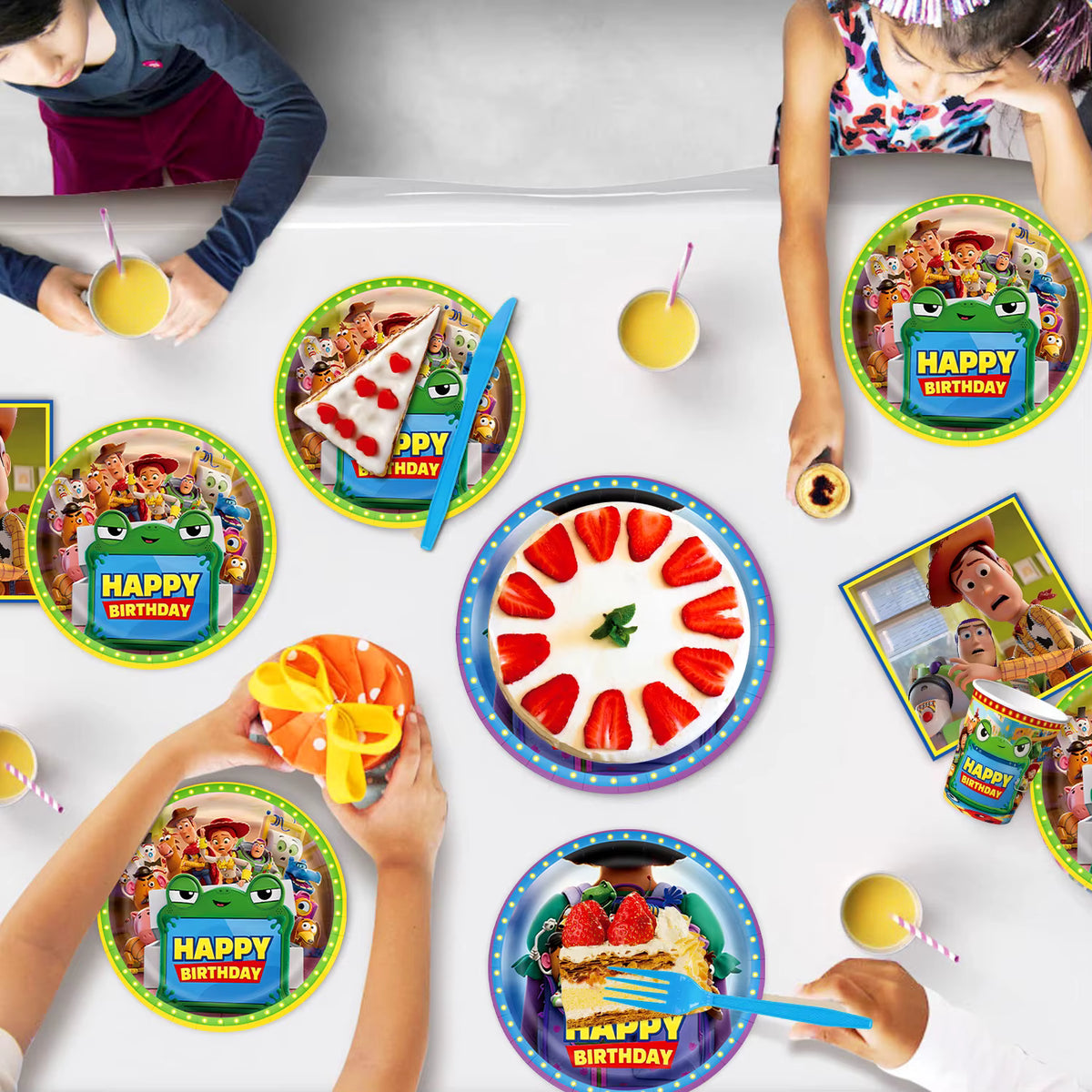 Enfants partageant un gâteau d'anniversaire sur une table décorée avec des assiettes et gobelets en carton sur le thème de l'univers des jouets.