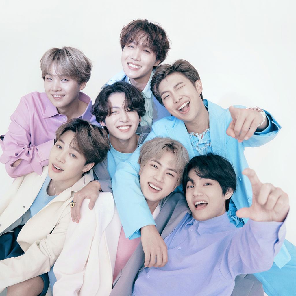 Les sept membres du groupe de K-Pop BTS souriants, posant de manière décontractée et vêtus de costumes aux couleurs pastel.