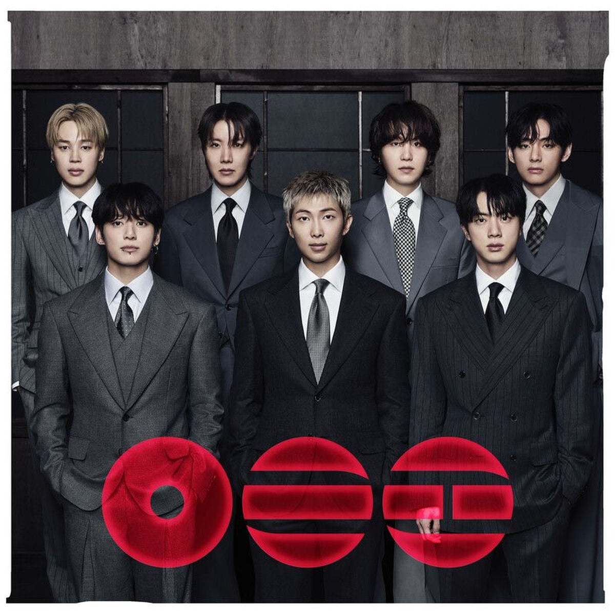 Le groupe sud-coréen BTS posant sérieusement en costumes gris foncés élégants, avec trois motifs circulaires rouges au premier plan.